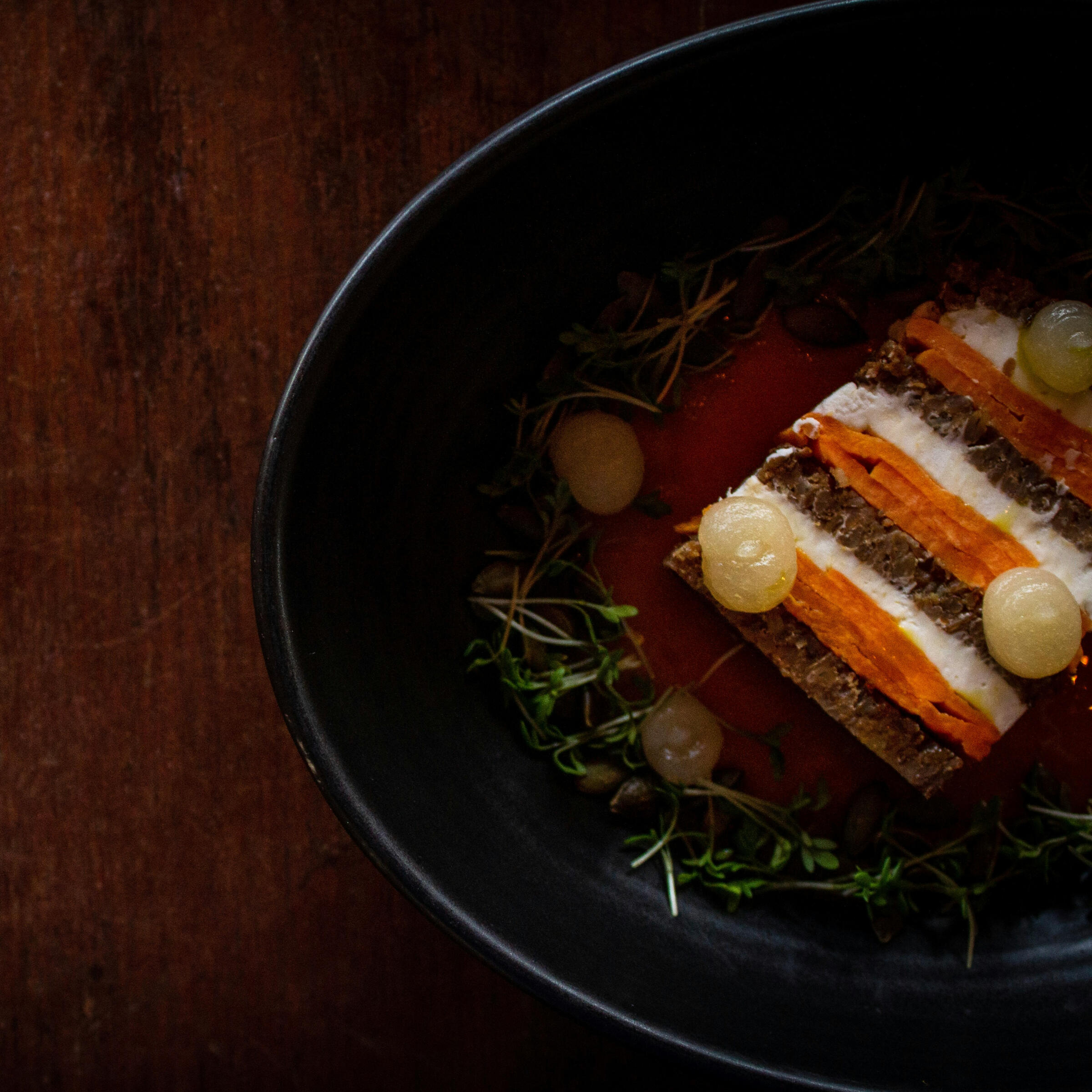 Plato de autor con capas de verduras y crema en plato negro, cocina creativa y equilibrada